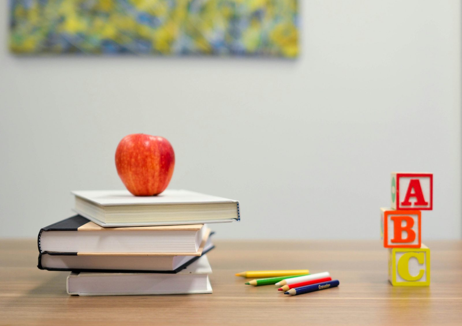 An apple on a stack of books, colored pencils and ABC blocks on a classroom desk